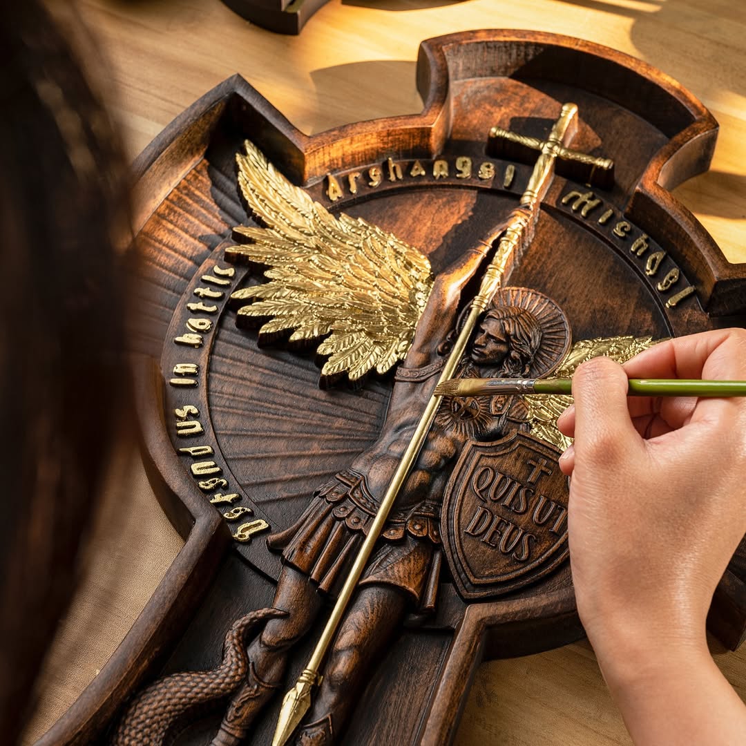 Mão aplicando acabamento dourado à mão em uma peça de arte sacra entalhada em madeira