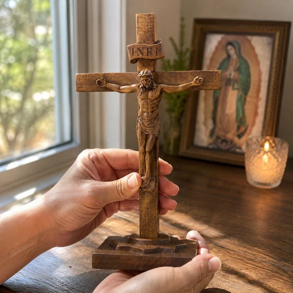 Crucifixo de Mesa em Madeira nas mãos com Nossa Senhora de Guadalupe ao fundo - Sagrado Tesouro